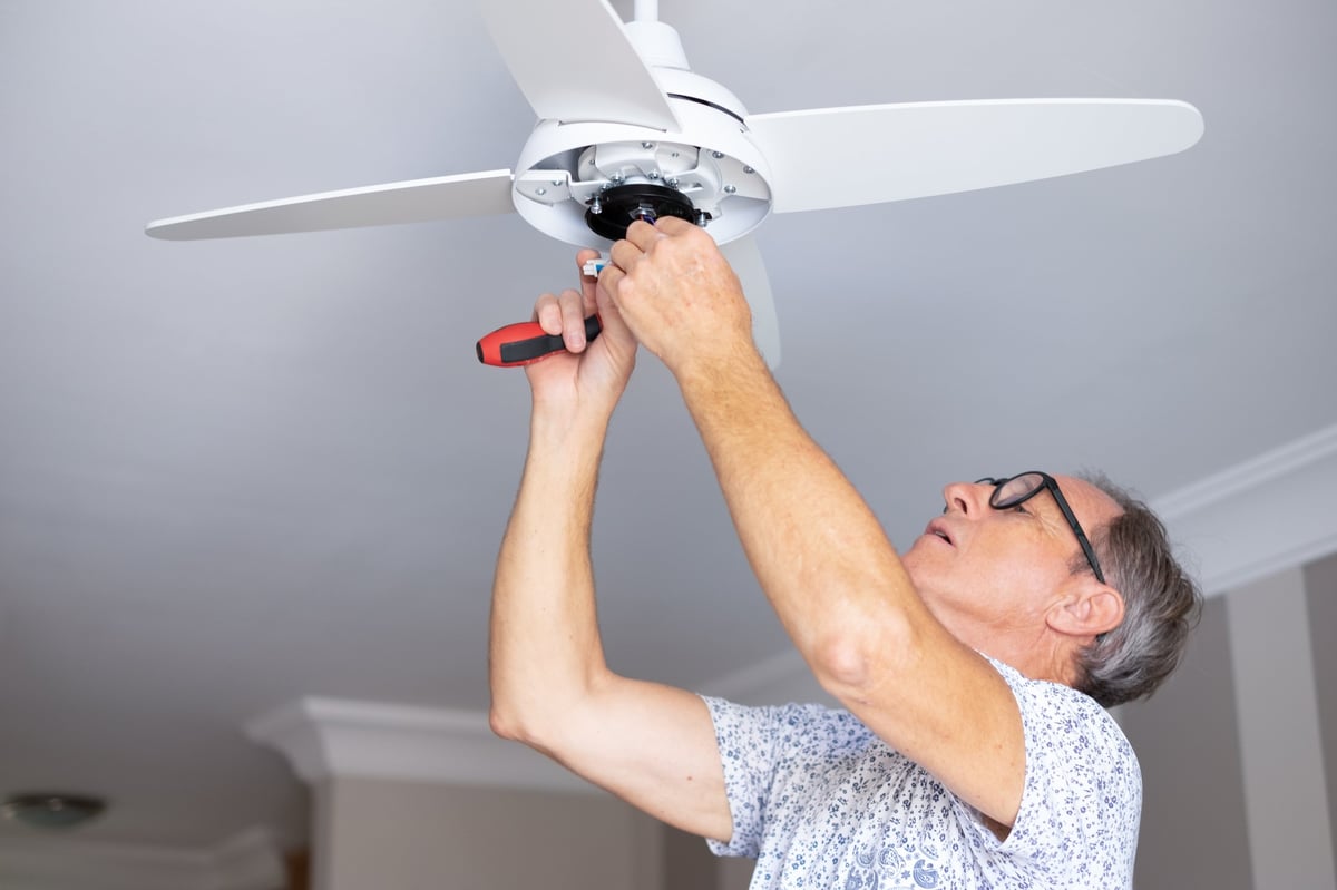 Technician on a ladder installing a ceiling fan in a Central Ohio living room